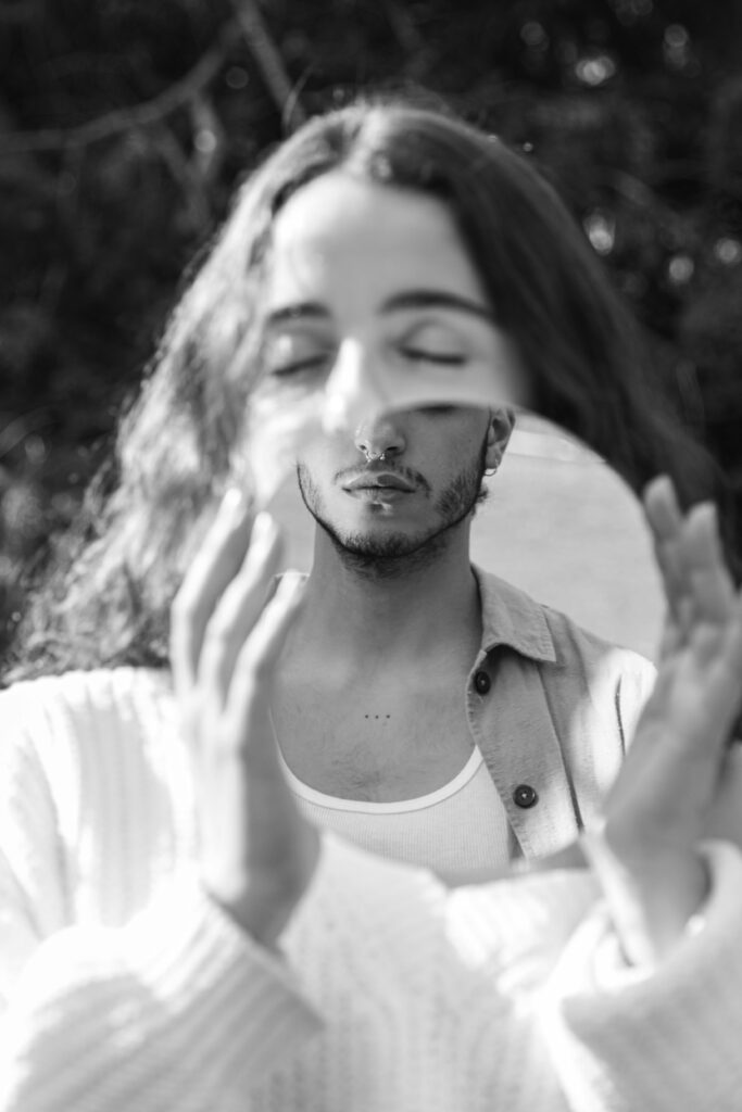 Black and white portrait of a person holding a mirror piece, reflecting their introspective expression.